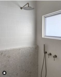 the shower head is next to the window in the bathroom with white tile on the walls