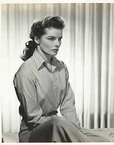 black and white photograph of a woman sitting on a bed with her legs crossed, looking off to the side