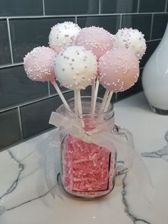 some pink and white cake pops in a jar on a counter with a glass vase