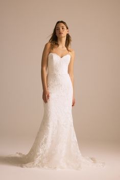 a woman in a white wedding dress standing against a beige background with her hands on her hips