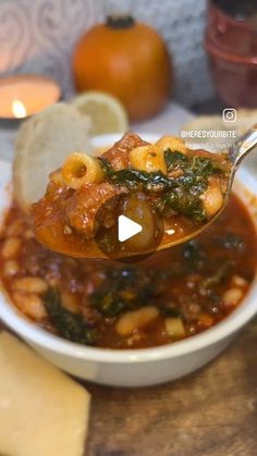 a spoon full of soup with spinach and cheese on the table next to some crackers