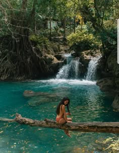 a woman sitting on a log in front of a waterfall