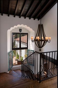 a chandelier hanging from the ceiling next to a wooden stair case in front of a window