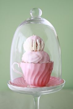 a pink cupcake under a glass dome on a cake plate with a saucer underneath it