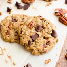 two cookies with pecans and chocolate chips are on a cutting board next to a bowl of pecans