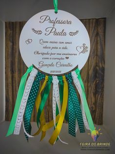 a white sign with green and yellow ribbons hanging from it's side, in front of a wooden wall