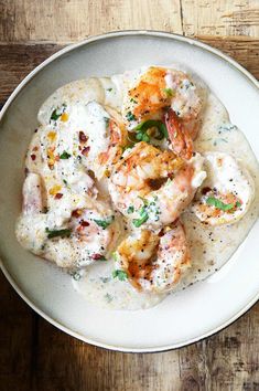 a white bowl filled with shrimp and grits on top of a wooden table next to a fork