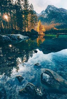 the sun shines brightly over a mountain lake surrounded by rocks and pine trees in the foreground