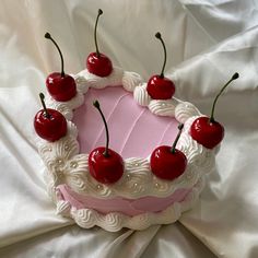 a cake with cherries on top is sitting on a white sheet and has pink frosting