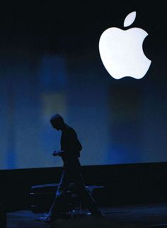 a man walks past an apple logo in front of the company's projected stage