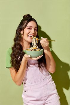 a woman in overalls eating noodles with chopsticks