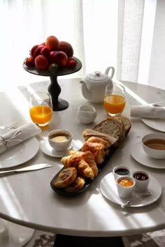 a table topped with plates and cups filled with breakfast food next to a bowl of fruit