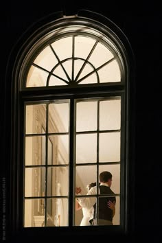 a bride and groom standing in front of a window at night