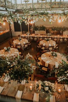 tables and chairs are set up for an event with greenery hanging from the ceiling