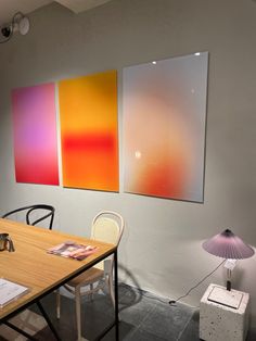 three paintings hang on the wall above a wooden table with two chairs and a lamp