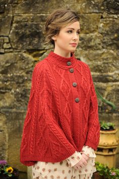 a woman standing in front of a stone wall wearing a red sweater and polka dot pants