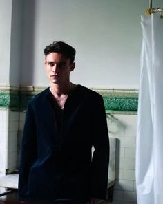 a man standing in front of a bathroom sink next to a white shower curtain and tiled walls