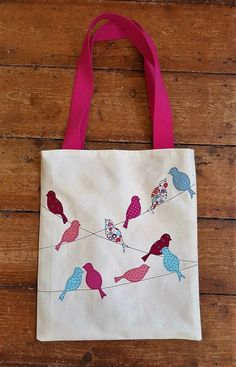 a white tote bag with birds sitting on a wire and pink ribbon hanging from it