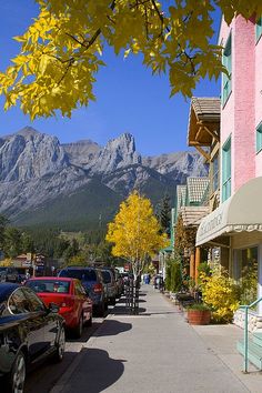 cars parked on the side of a street next to tall buildings with mountains in the background