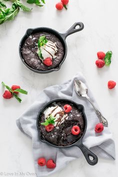 two black puddings with raspberries and ice cream in them on a white surface