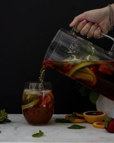 a person pouring liquid into a pitcher filled with fruit