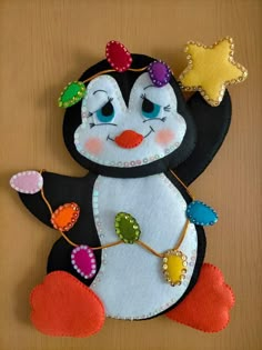 a felt penguin is sitting on top of a wooden table and has decorations around its neck