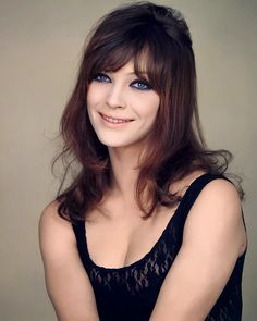 a woman with blue eyes is posing for the camera and smiling at the camera while wearing a black dress