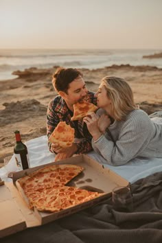 a man and woman eating pizza on the beach