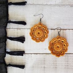 two wooden earrings with tassels hanging from them on a white table next to a black scarf