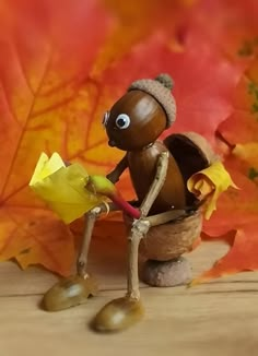 a small figurine sitting on top of a wooden table next to autumn leaves