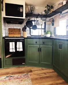 a kitchen with green cabinets and black appliances in the corner, along with a rug on the floor