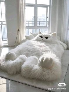 a large white cat laying on top of a bed in front of a big window