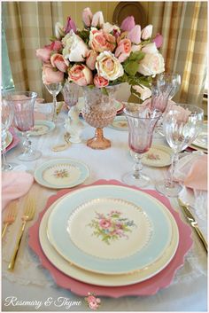 the table is set with pink and white plates, silverware, and flowers in vases