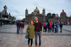 a man and woman standing in front of a large building with many people around it