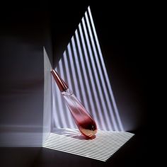 a red vase sitting on top of a table next to a window with vertical blinds