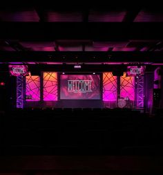 the stage is lit up with purple and red lights for a welcome sign on it