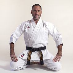 a man sitting on the ground wearing a white karate suit and black belt with his hands behind his back