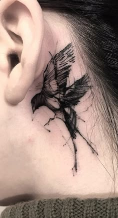 a woman's behind the ear has a black bird tattoo on her left side