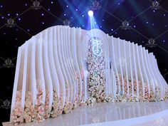 the stage is decorated with white curtains and pink flowers, while blue lights shine in the background