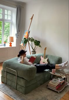 a woman sitting on top of a green couch in a living room next to a window