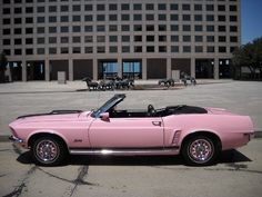 a pink convertible car parked in front of a large building