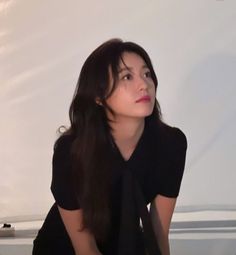 a woman with long dark hair sitting on the floor in front of a white wall