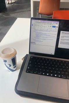 an open laptop computer sitting on top of a white table next to a cup of coffee