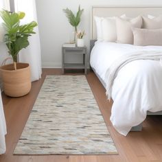 a white bed sitting next to a green plant on top of a hard wood floor