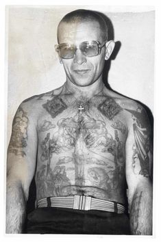 a man with many tattoos on his chest and arms is standing in front of a wall