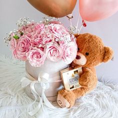 a teddy bear sitting next to a bouquet of flowers and balloons in a hat box