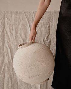 a person holding a large white vase on top of a cloth covered tableclothed wall