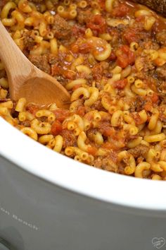 a wooden spoon is in a slow cooker filled with macaroni and cheese