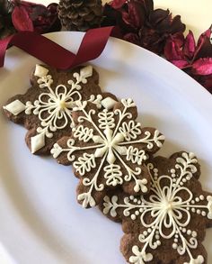 three decorated cookies on a white plate with a red ribbon