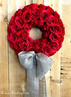 a red rose wreath hanging on the side of a wooden wall with a gray ribbon